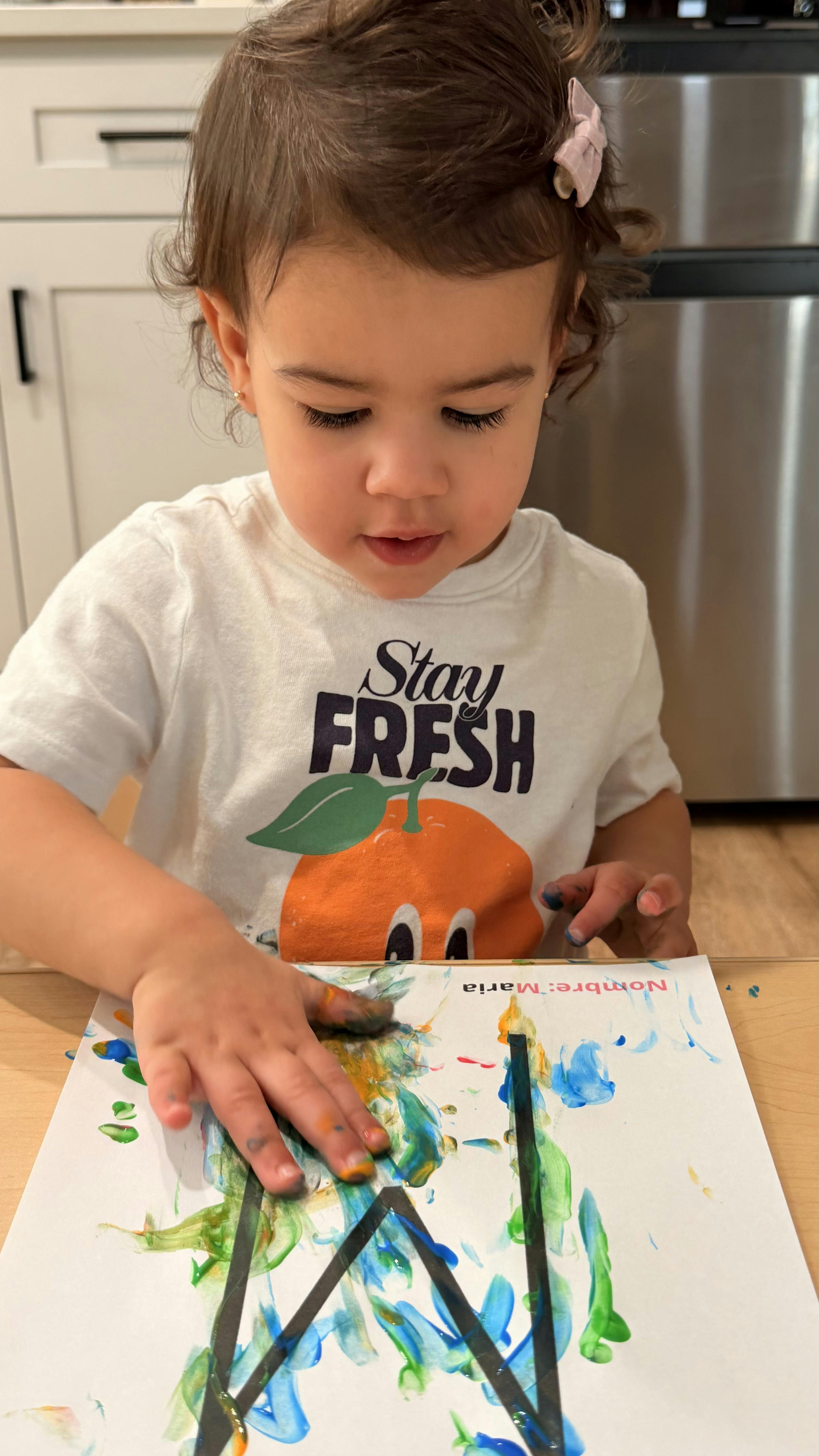 Child finger painting a colorful design on white paper