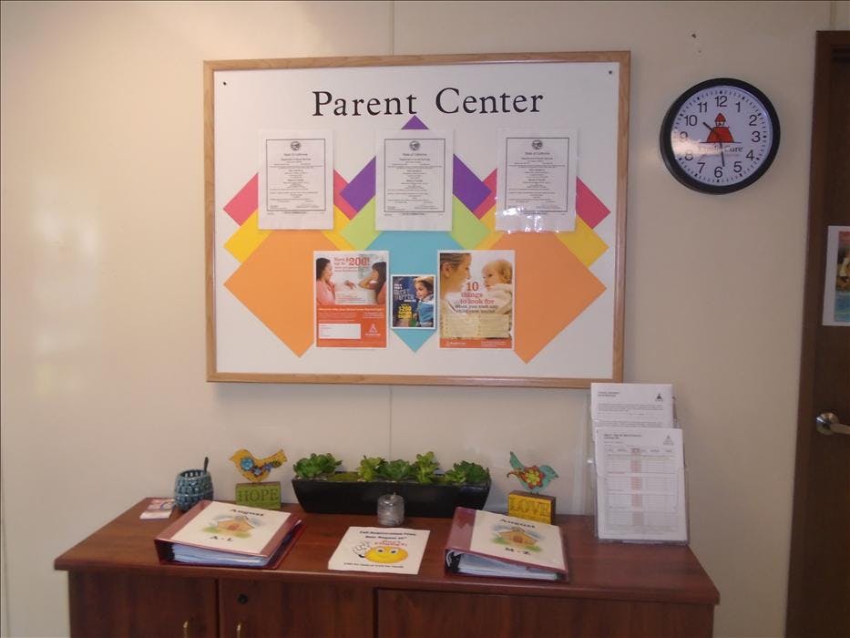 A Parent Center bulletin board with papers, flyers, and a clock above a wooden cabinet
