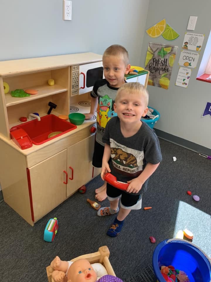 Two children playing in a classroom with a toy kitchen