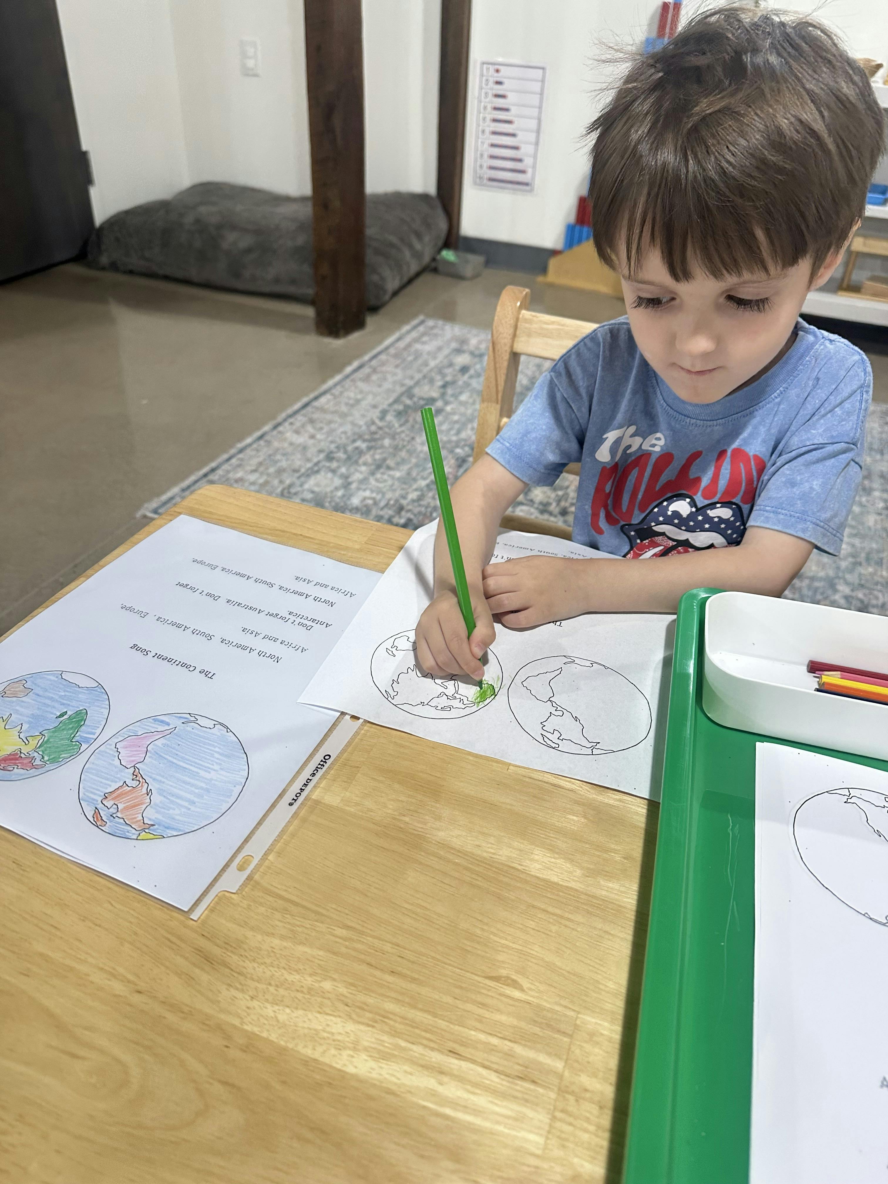 Child coloring a picture of a globe on a piece of paper at a wooden table