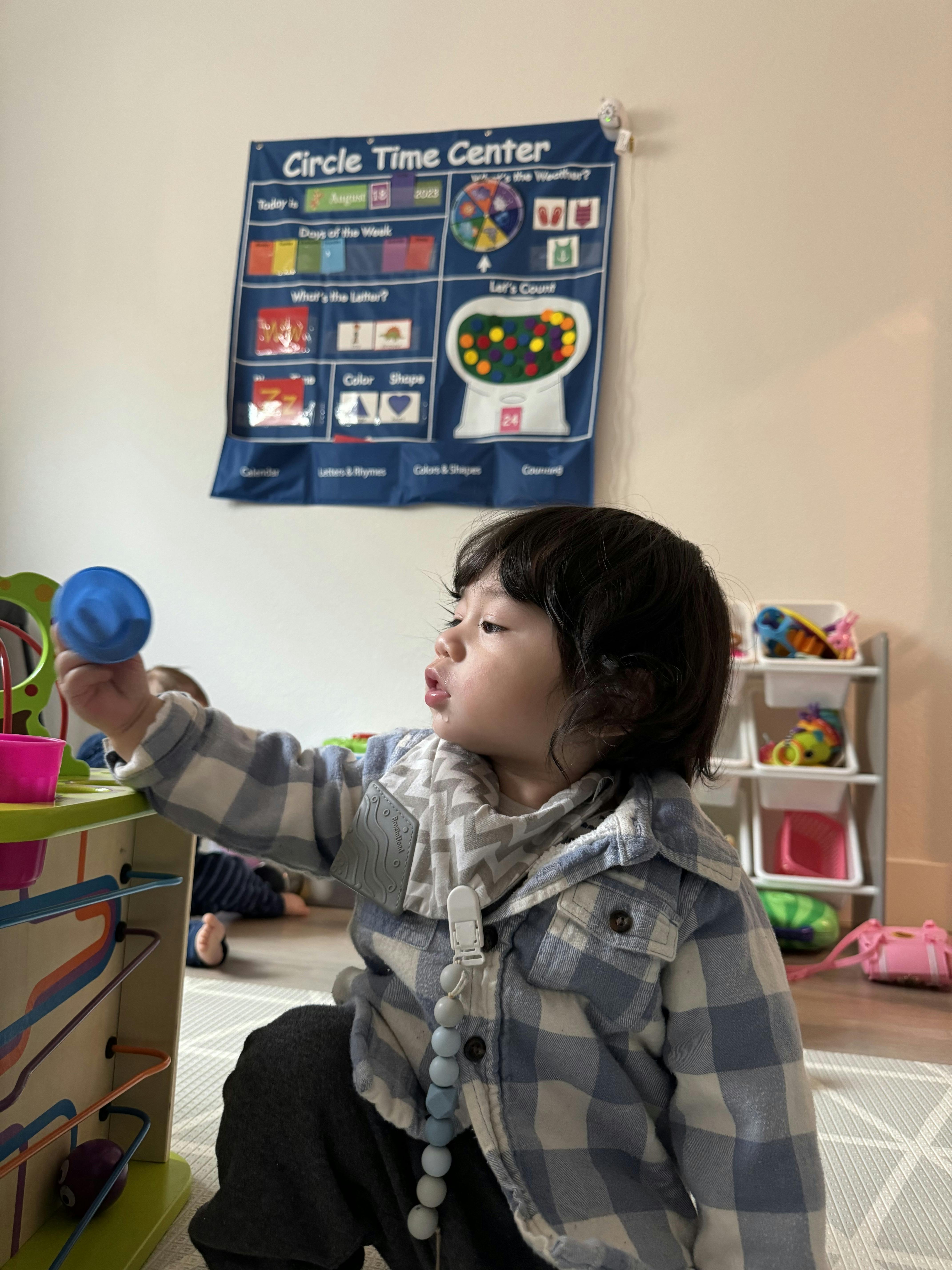 Child playing with a blue toy and a wooden activity center