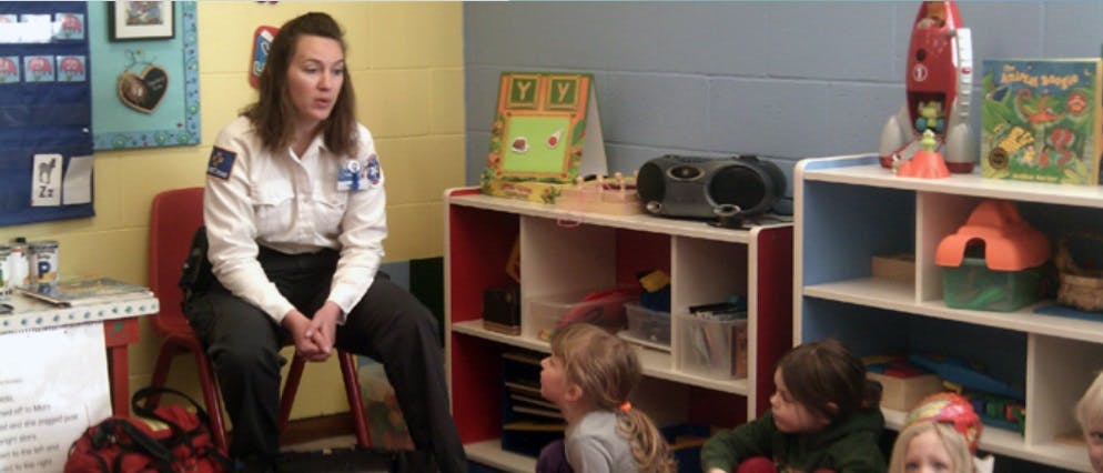 Person in uniform sitting on a chair in a classroom with children