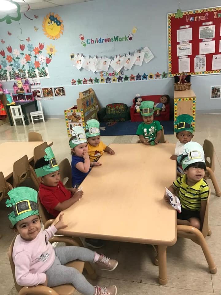 Children wearing green hats sitting around a table in a classroom