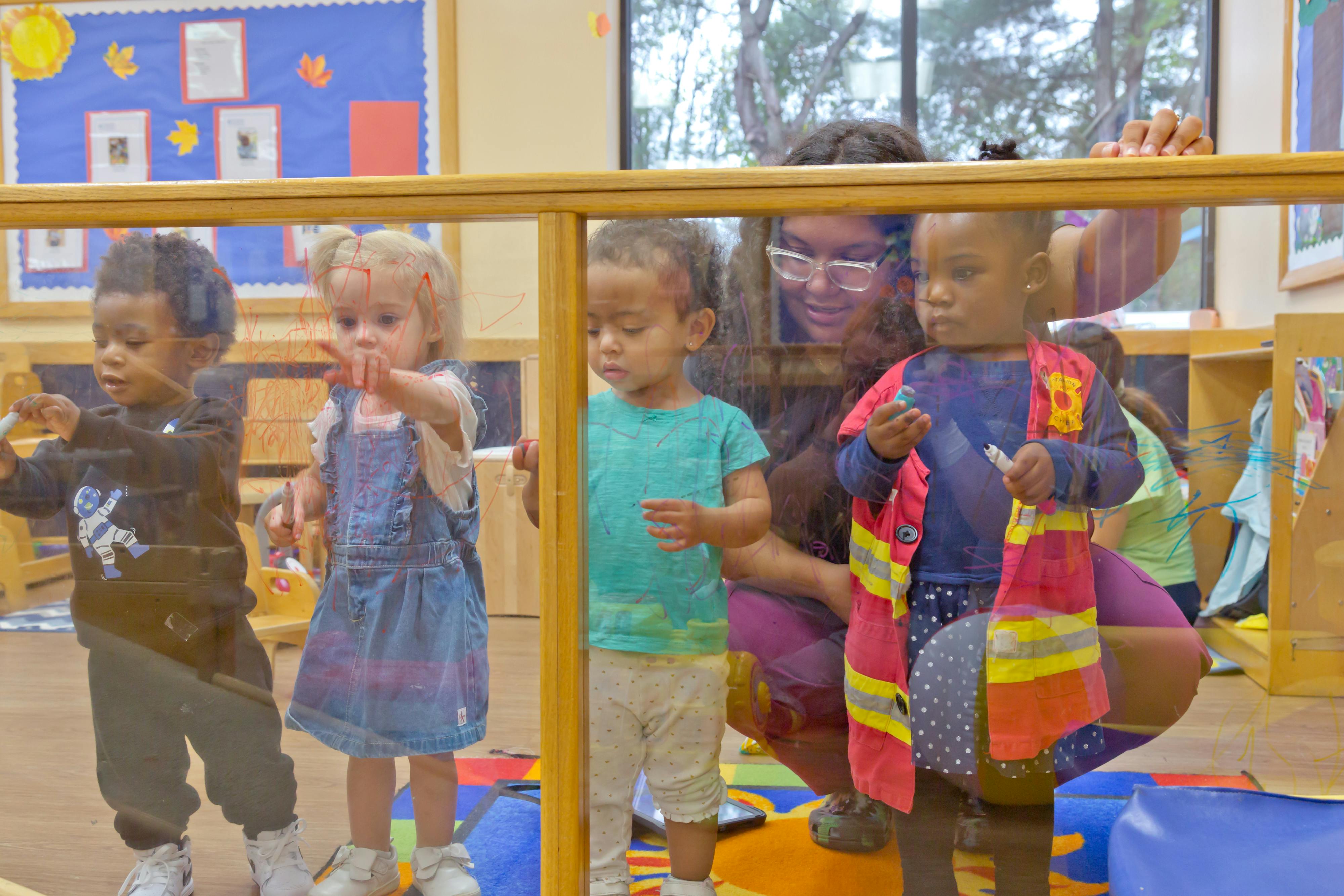 Adult and children looking through a clear barrier in a classroom