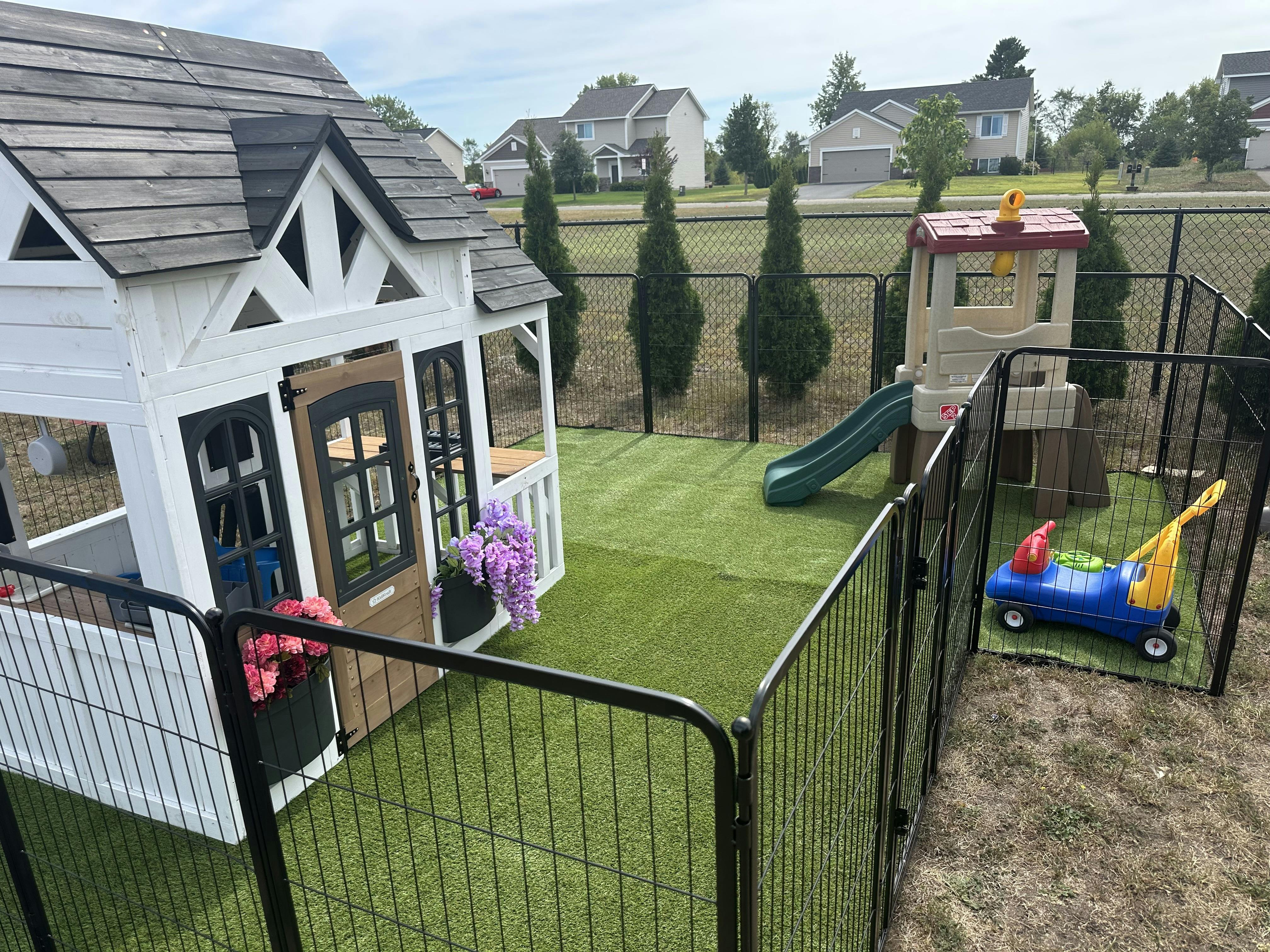 Childrens playhouse and playground equipment in a fenced yard