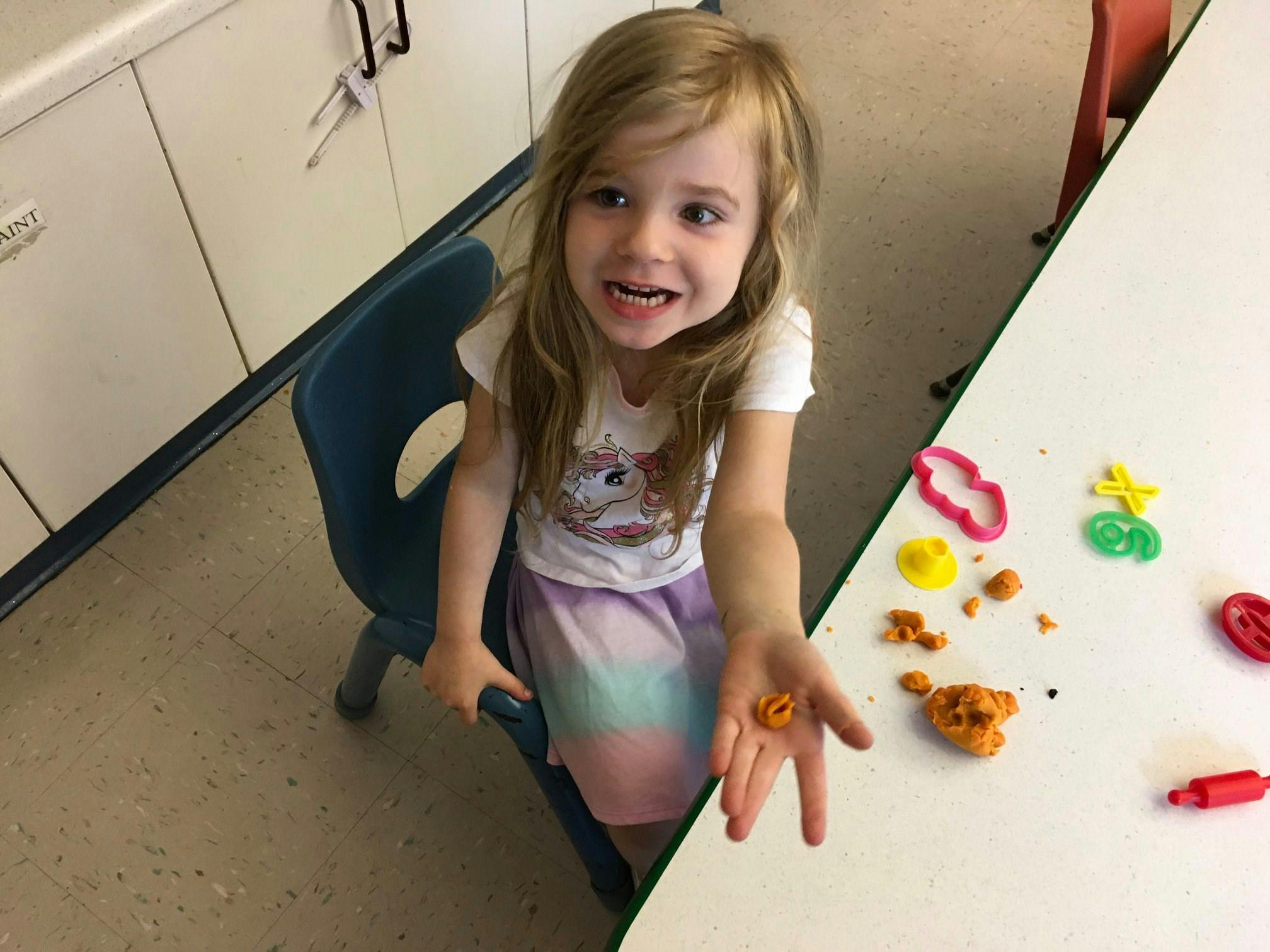 Child sitting at a table holding a small piece of playdough