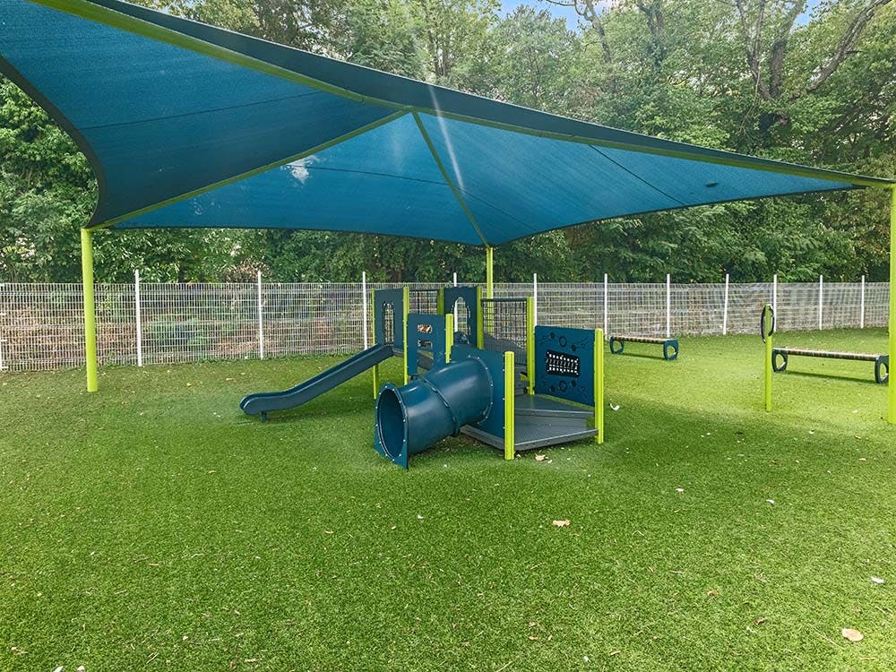 Playground with blue shades, slides, and tunnel on green turf