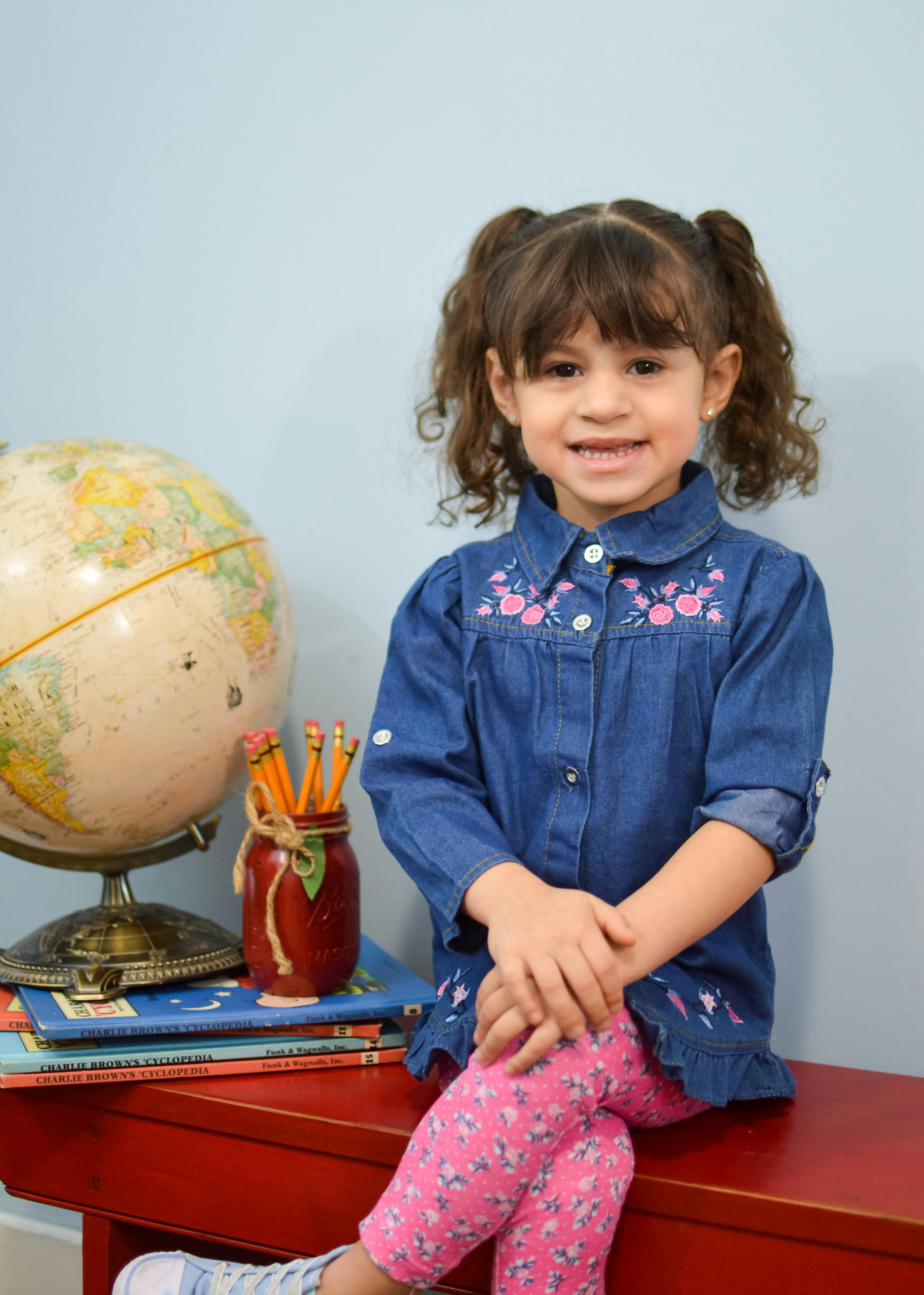Child sitting on a red bench next to a globe and a jar of pencils