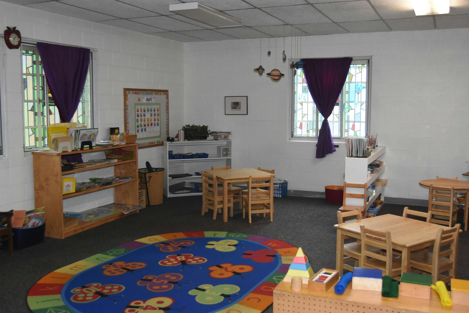 Classroom with small tables and chairs, shelves, and a colorful rug