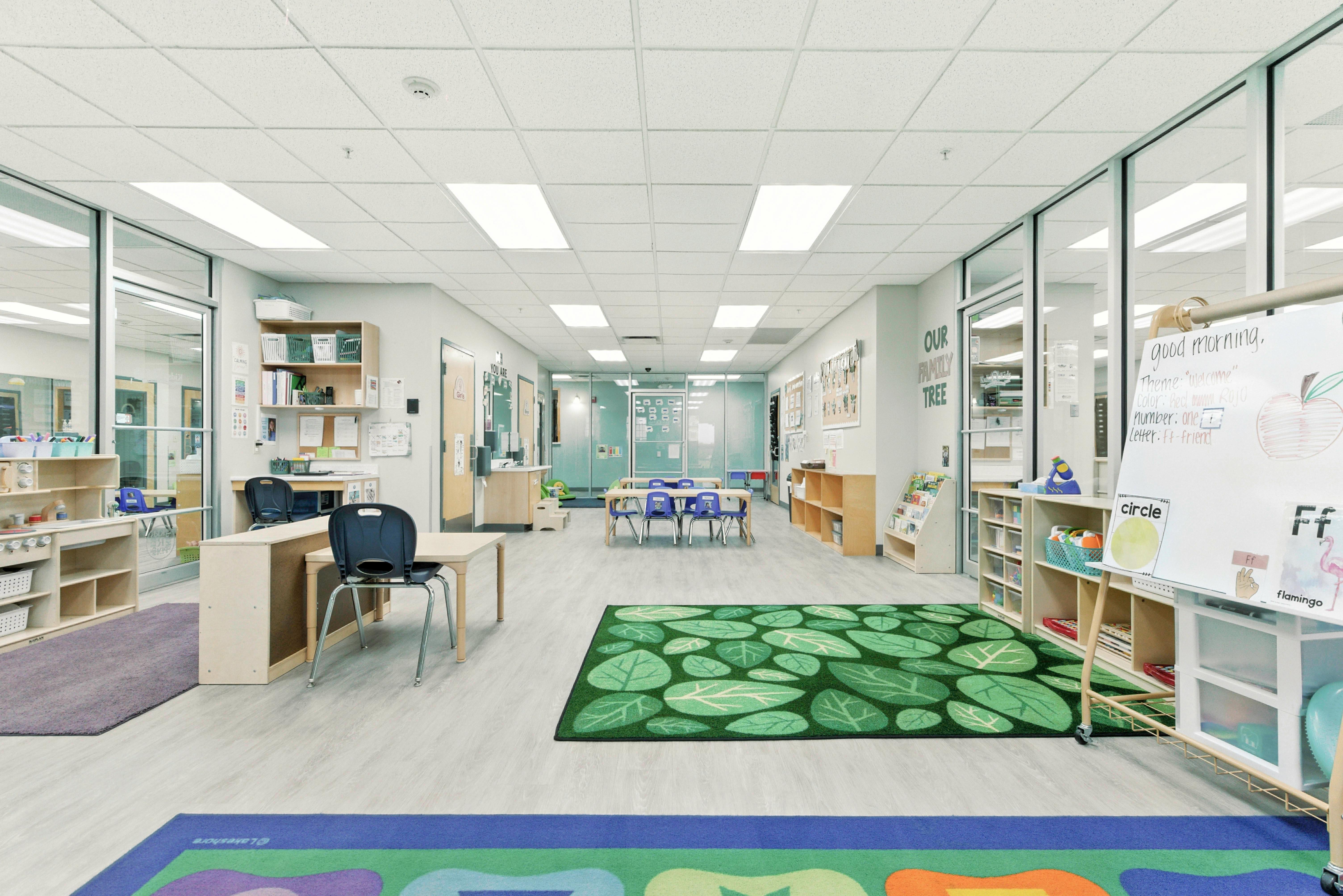 Empty classroom with tables, chairs, and a green rug