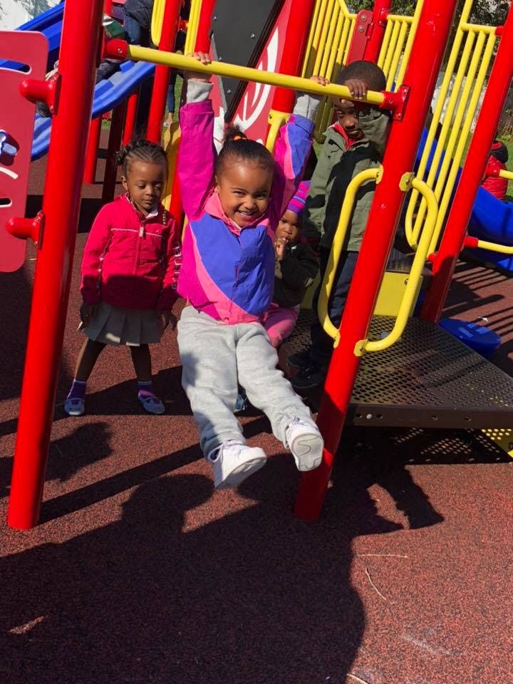 Child hanging from a yellow bar on a playground structure