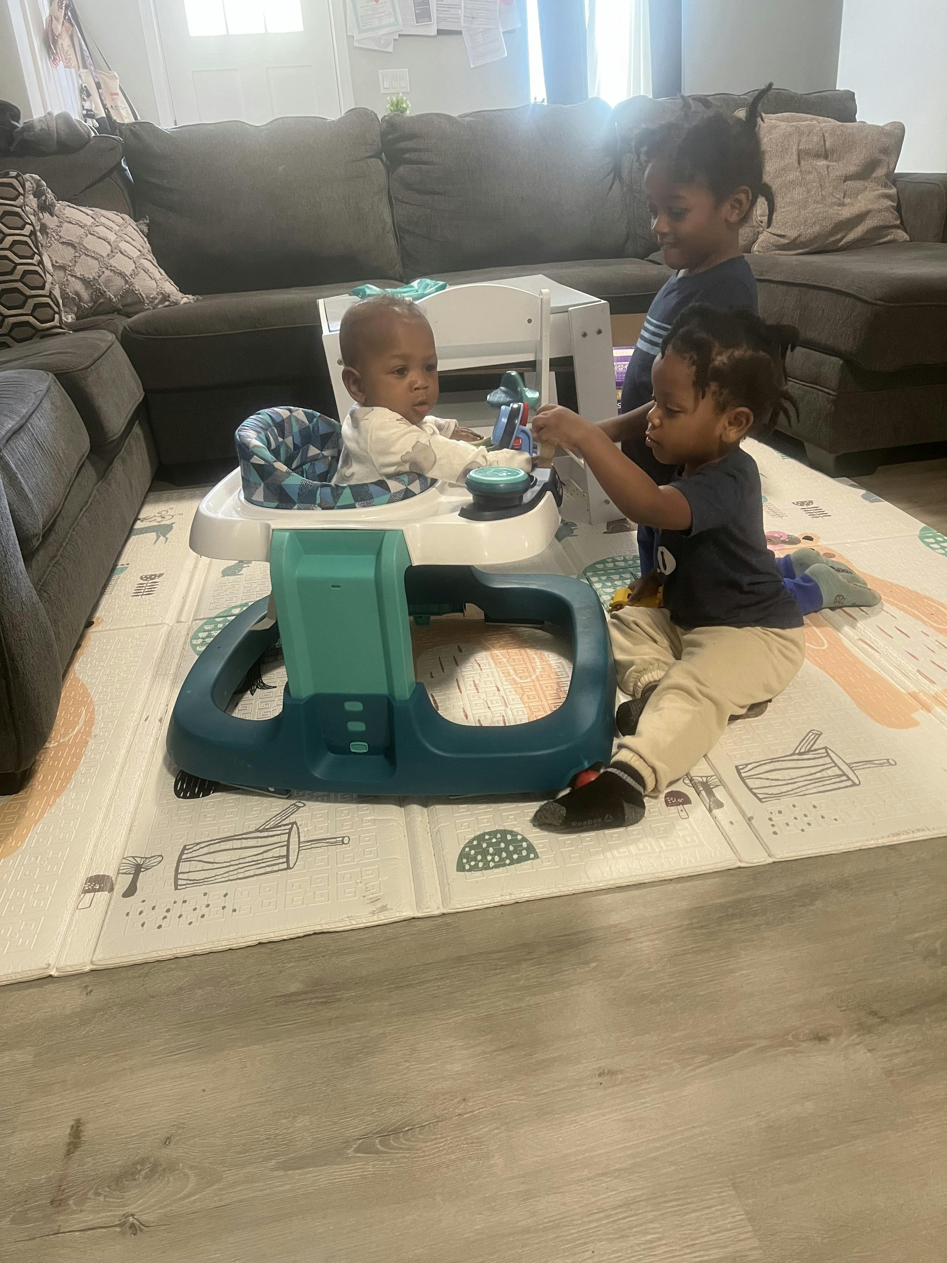 Three children playing on a mat, one in a baby walker