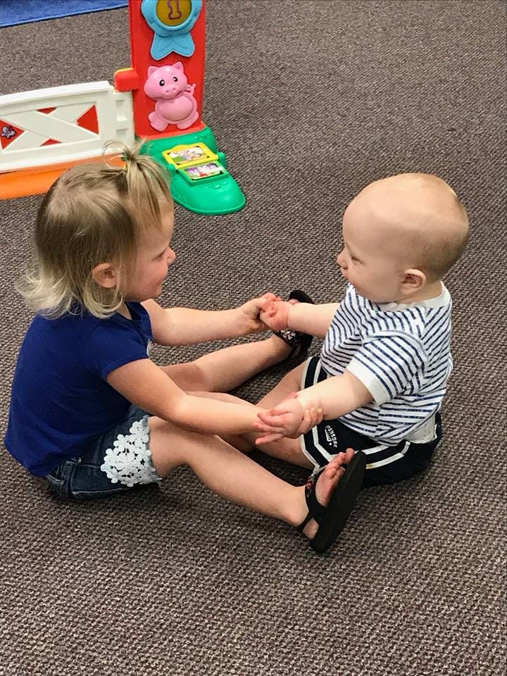 Child and baby sitting on floor holding hands