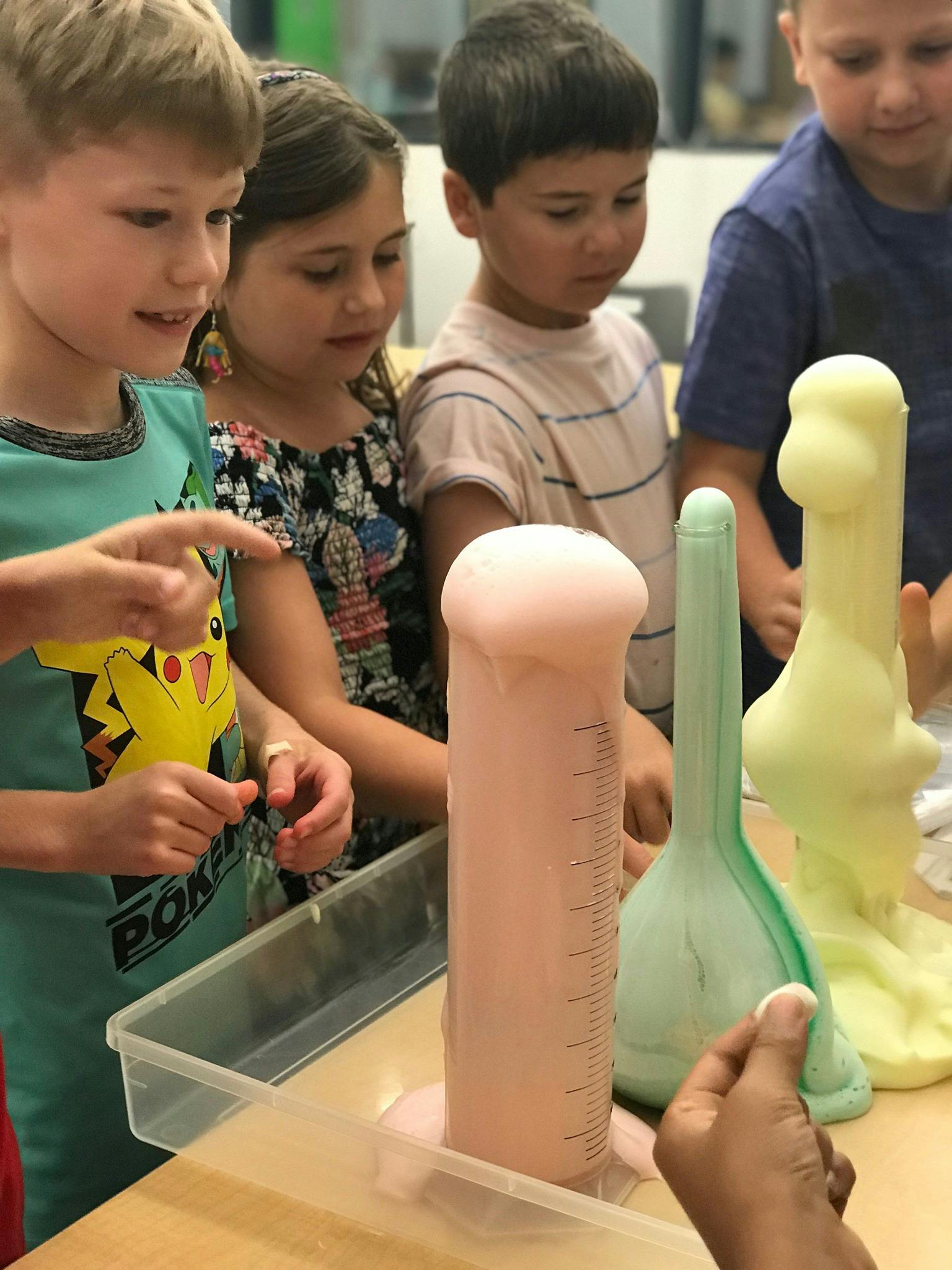 Children watching a science experiment with foam erupting from cylinders