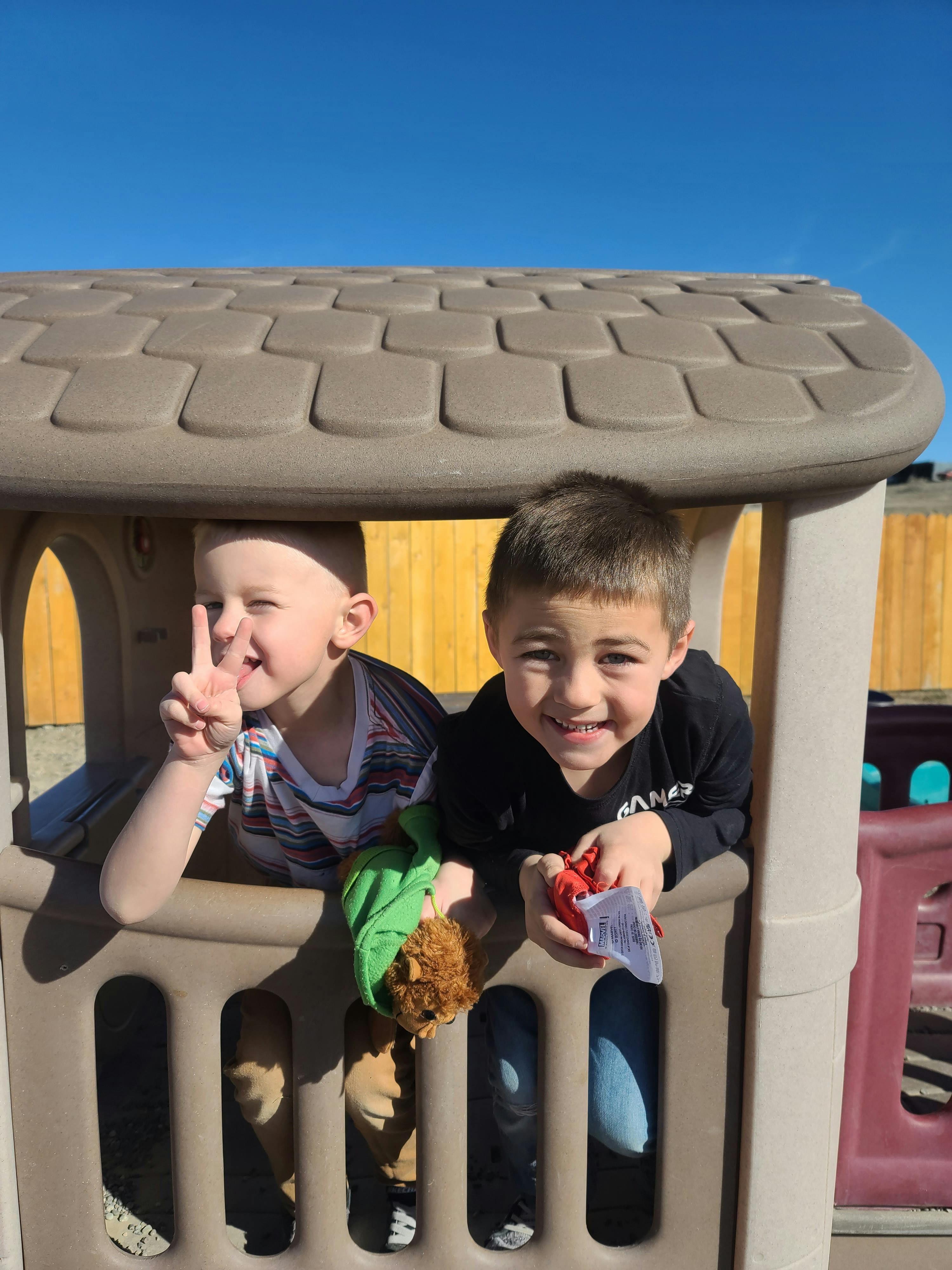 Two children in a playhouse, one making a peace sign