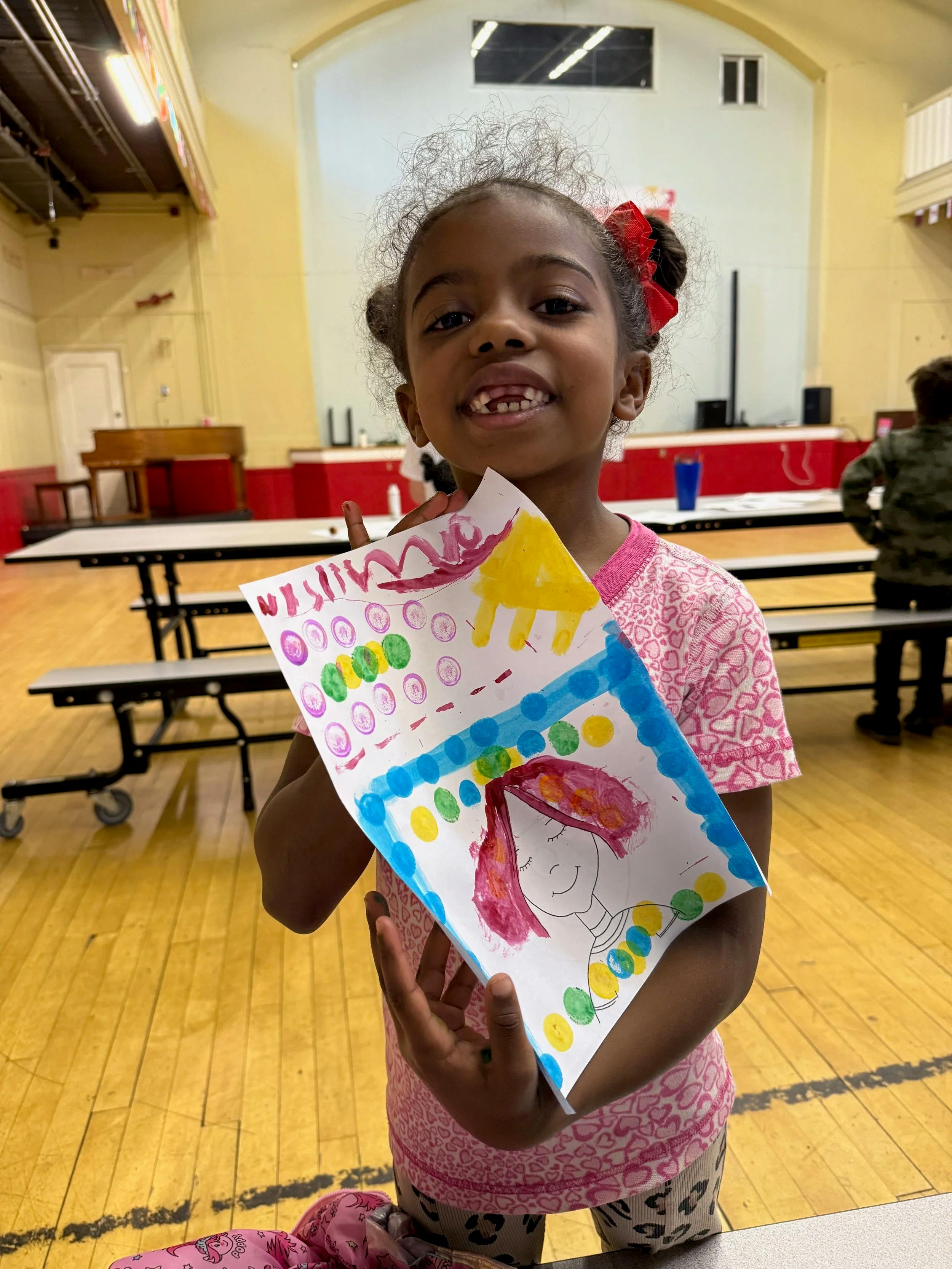 Child smiling while holding up a colorful drawing