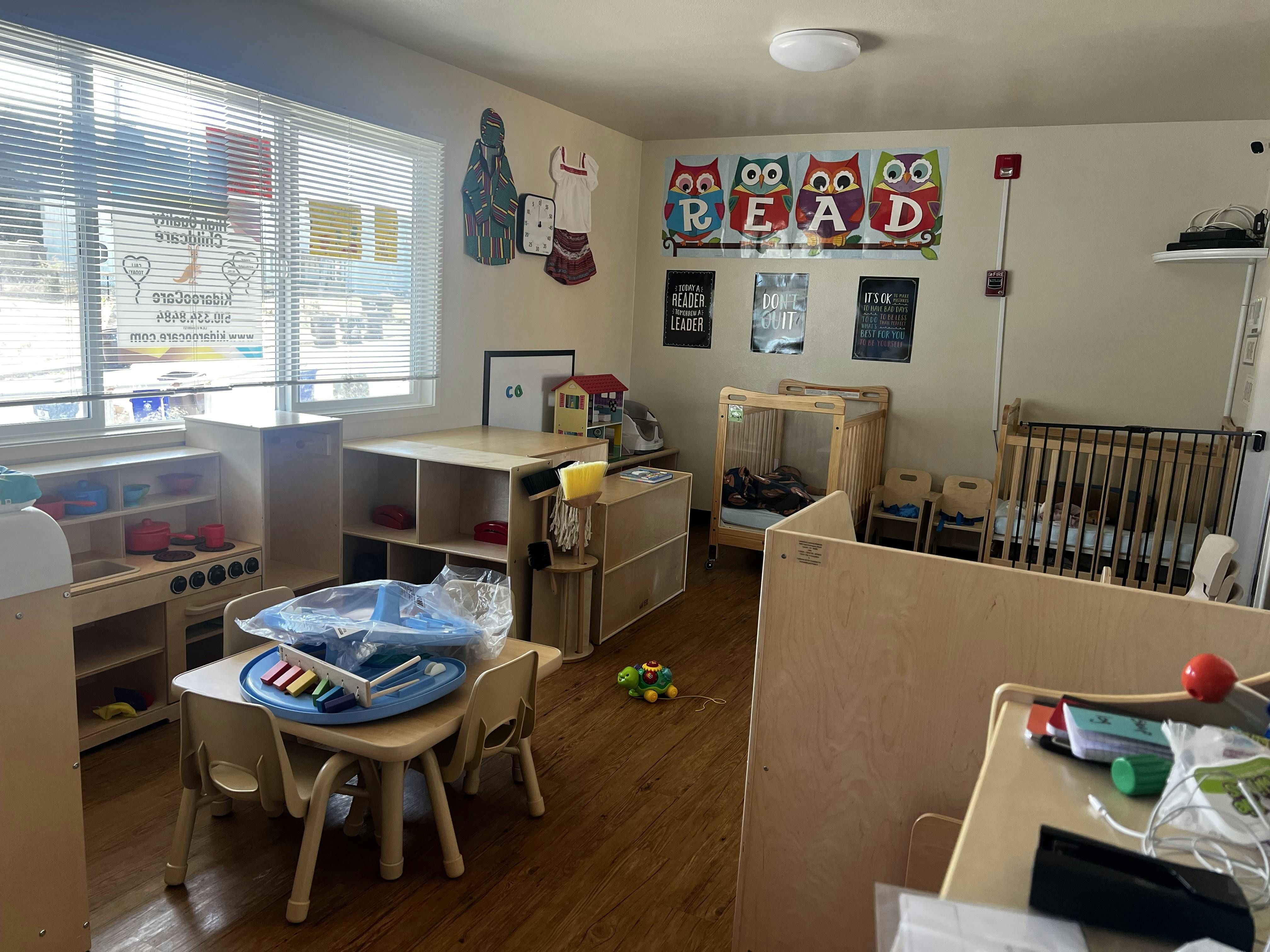 A classroom with small tables, chairs, and cribs, with a "READ" sign on the wall