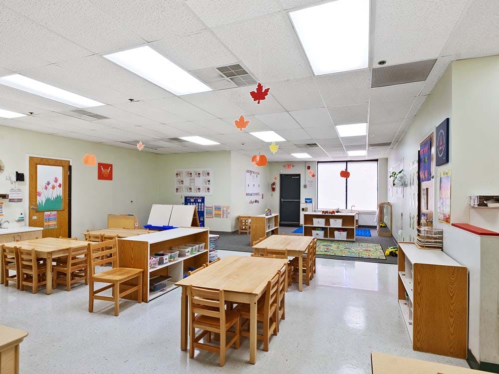 Empty classroom with small wooden tables and chairs, decorated with fall-themed cutouts