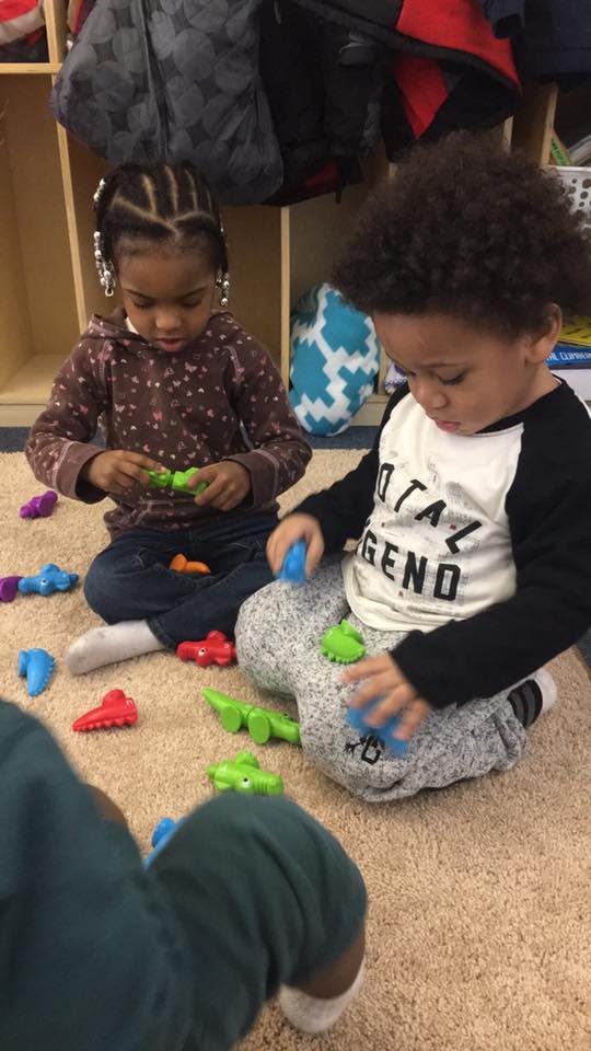 Two children sitting on a carpet playing with colorful plastic toys