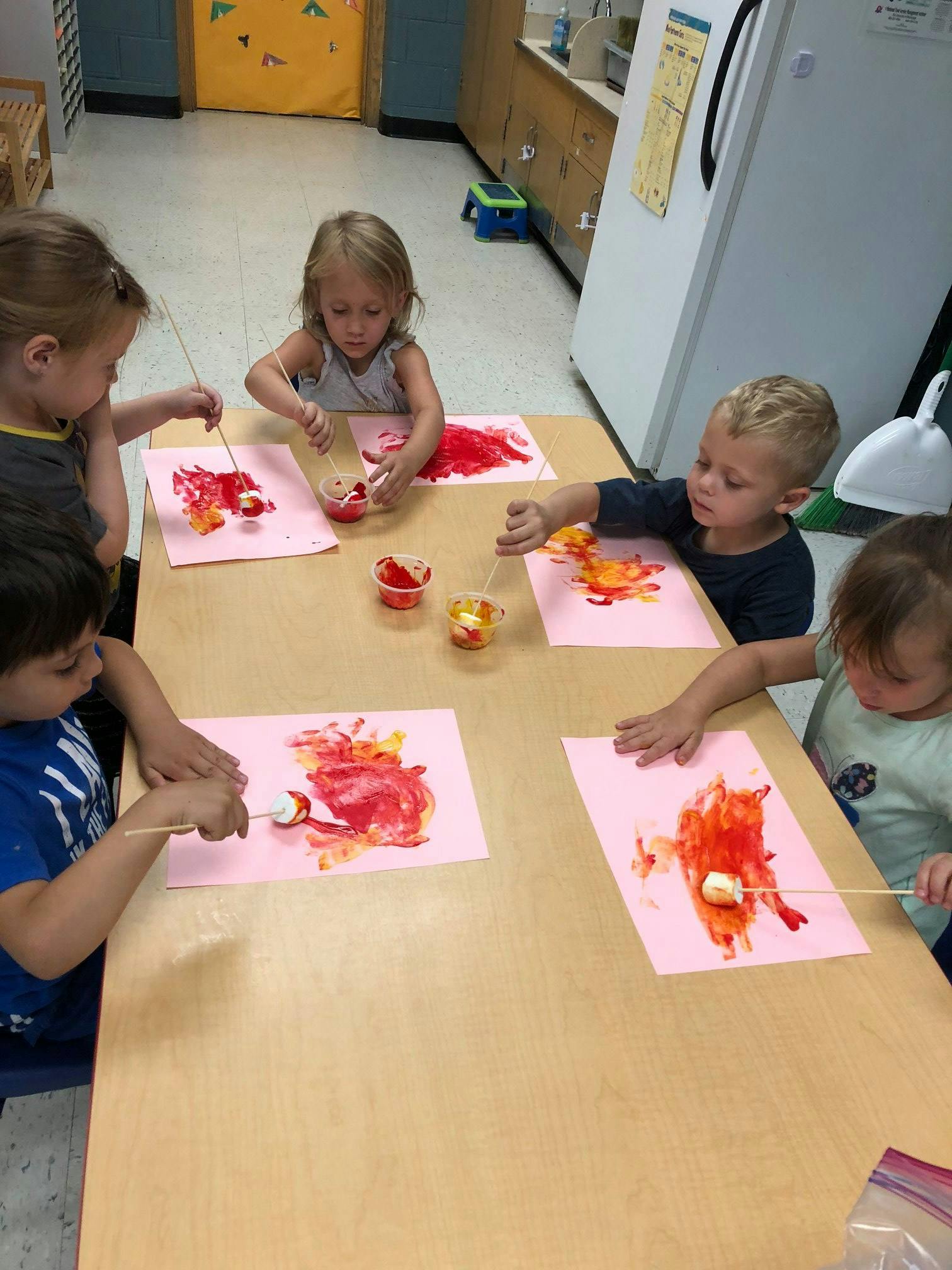 Children painting with marshmallows on sticks in a classroom