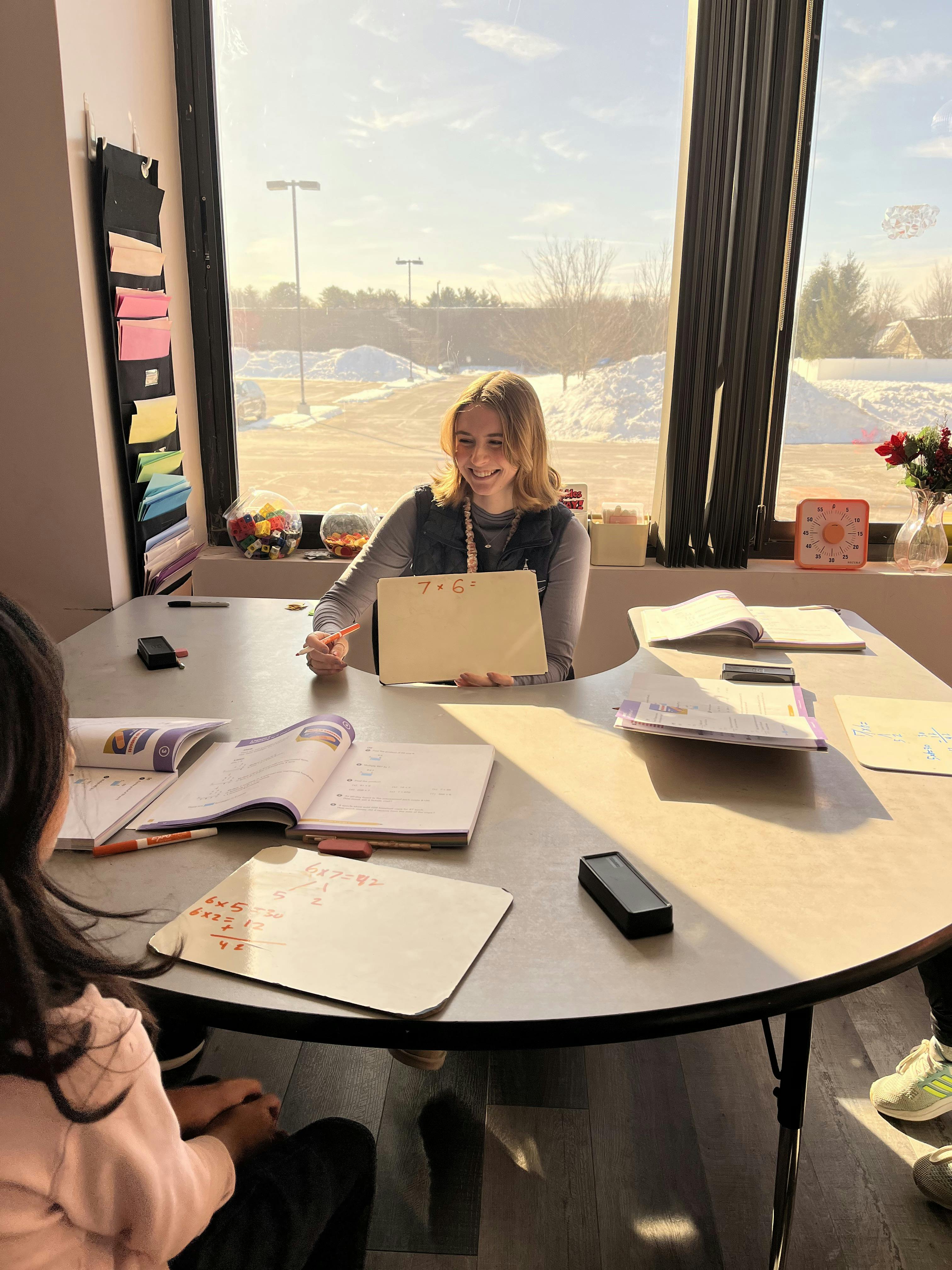 Person holding up a whiteboard with \"7x6=\" written on it during a math lesson