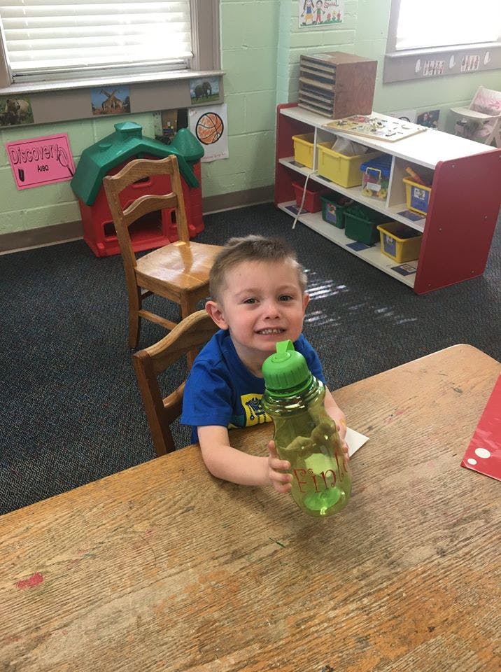 Child sitting at a table holding a water bottle in a classroom