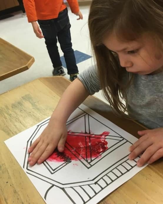 Child finger painting with red paint on a geometric drawing