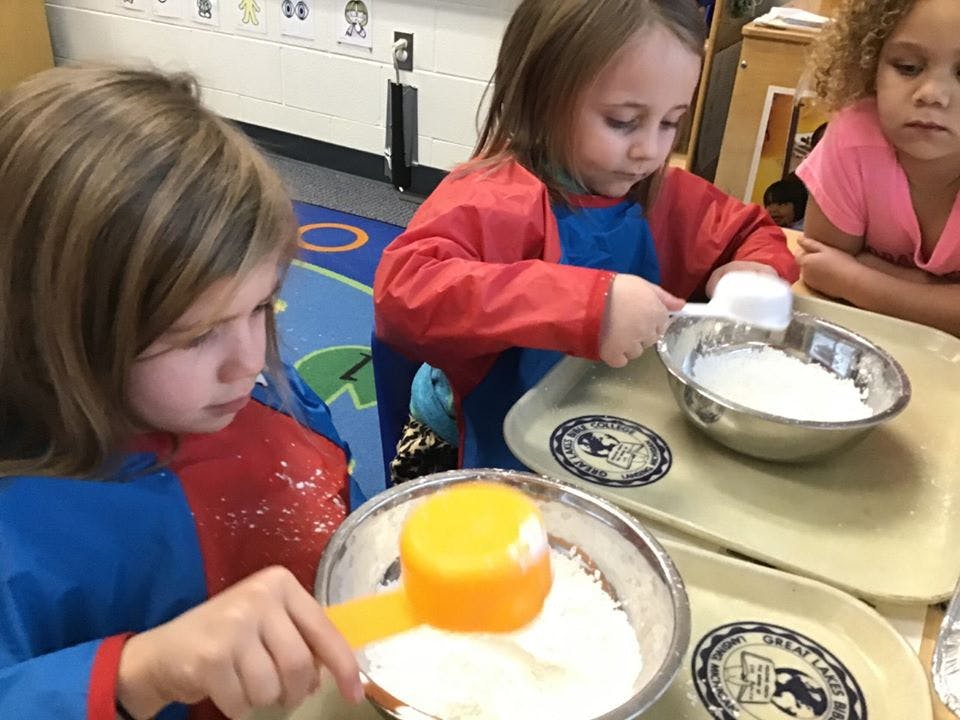 Two children in aprons scooping white powder from bowls