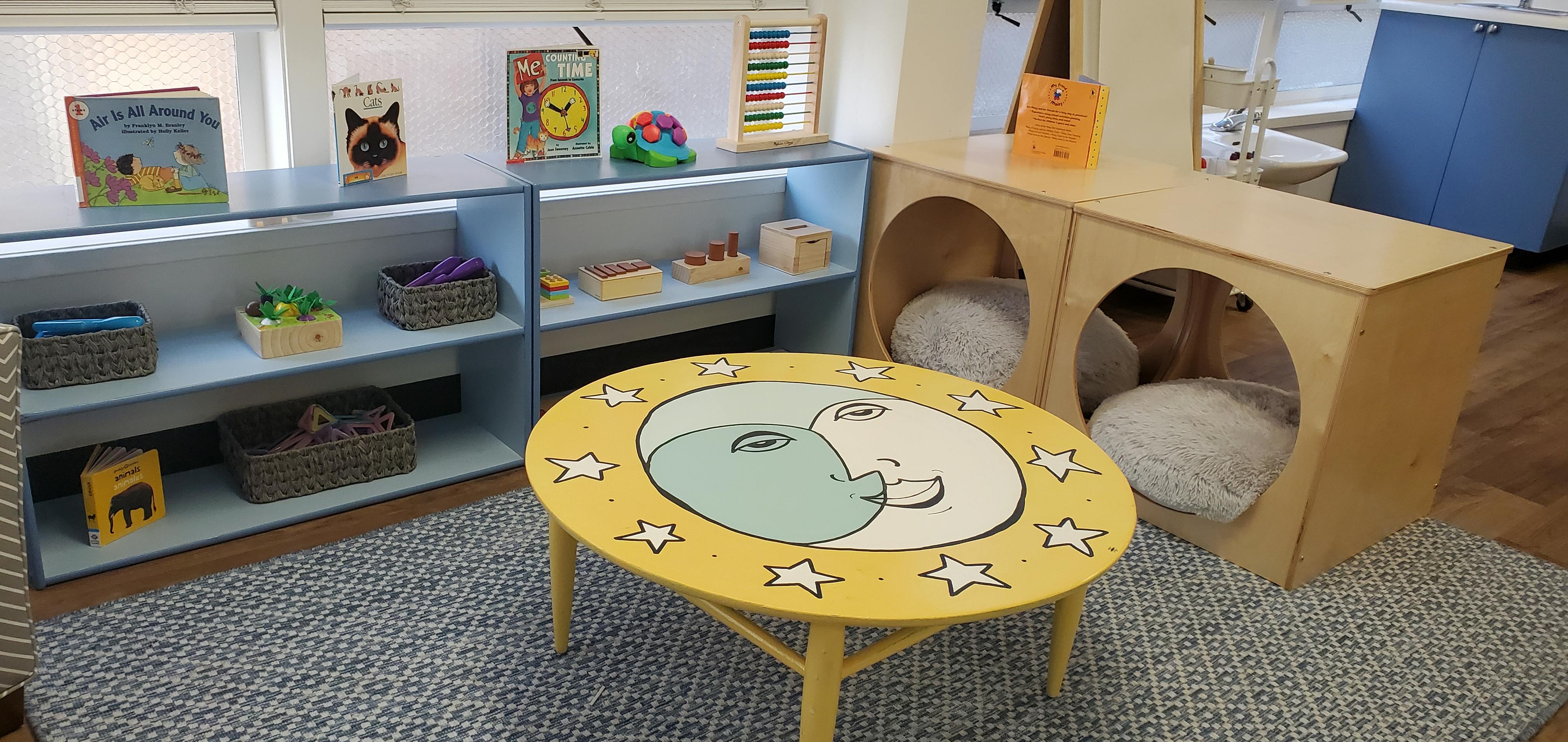 Classroom with shelves of toys, a yellow table, and wooden cubbies