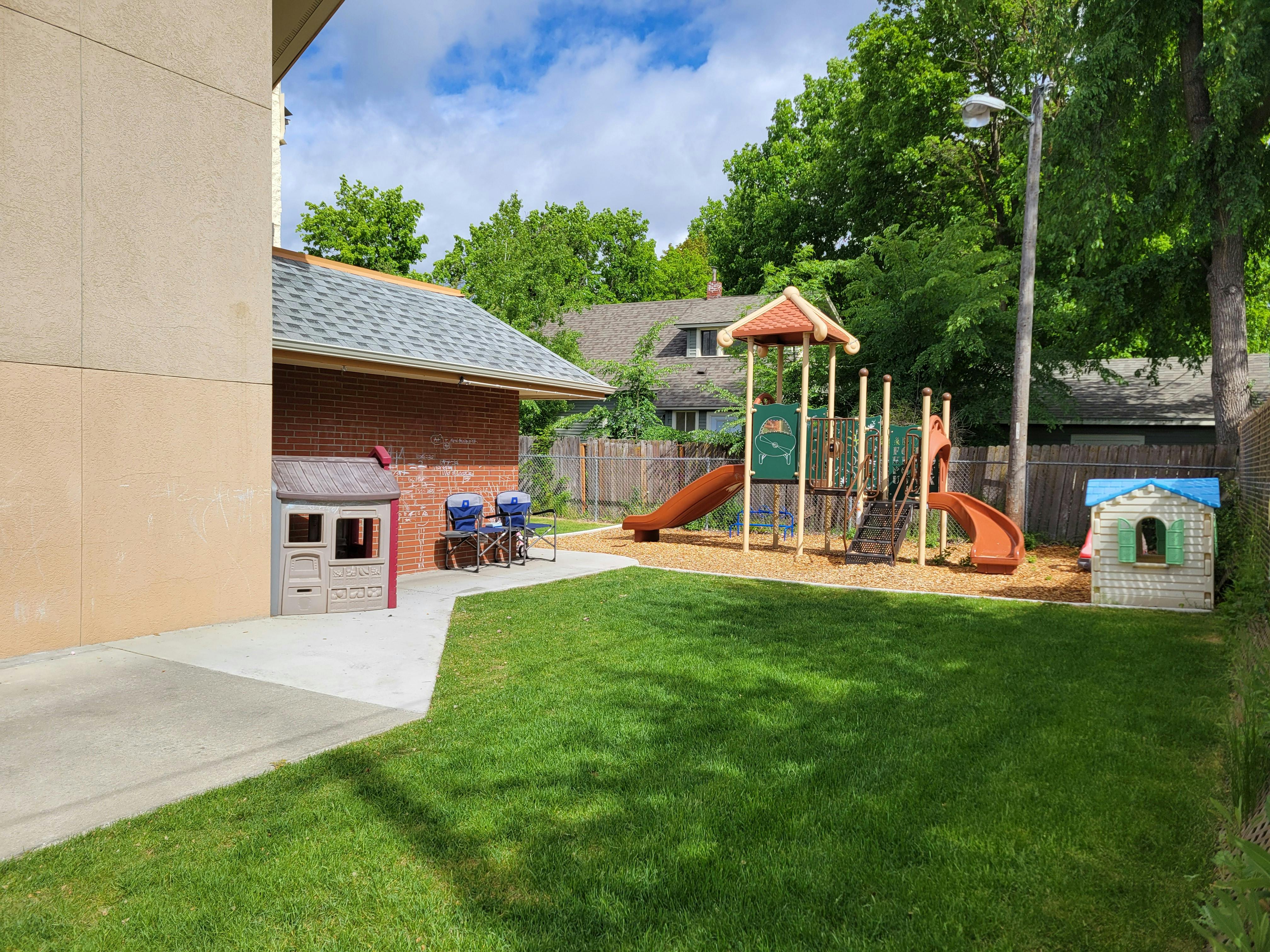Outdoor playground with slides, stairs, and playhouses next to a building