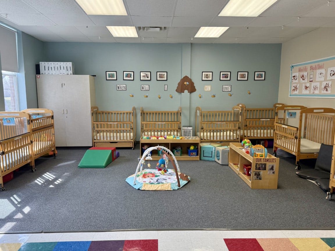 An empty nursery room with multiple cribs, a playmat, and shelves with toys