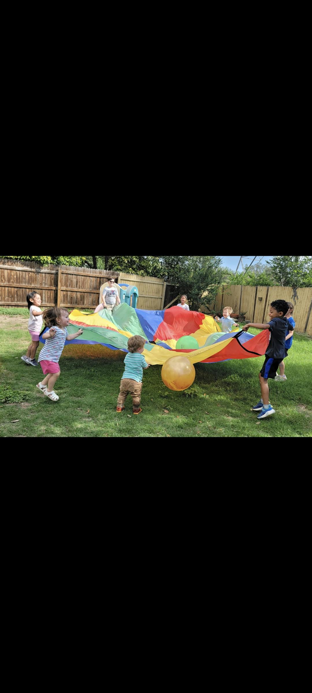Children playing with a rainbow parachute on a grassy lawn