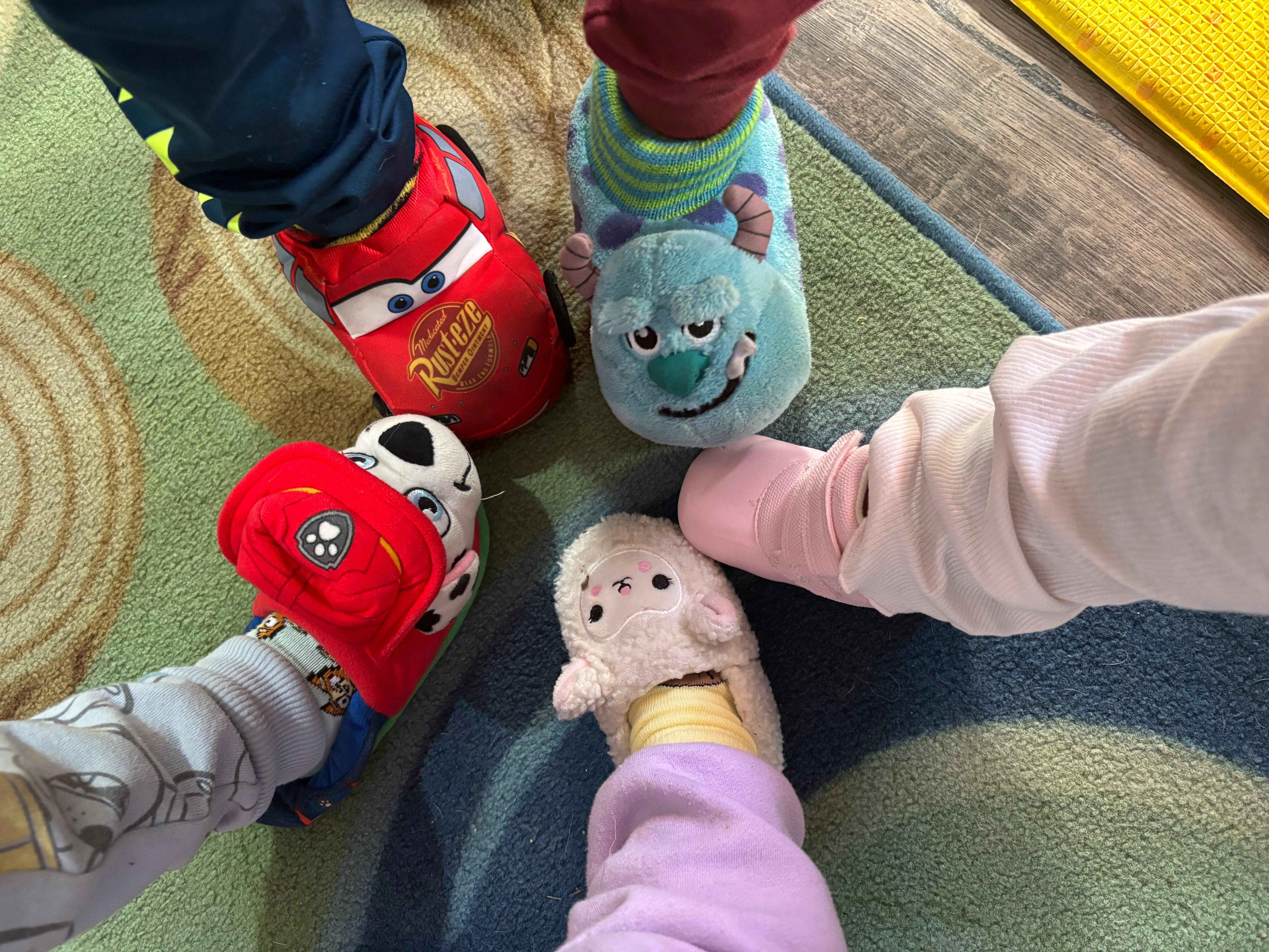 Four children's feet in a circle wearing various character slippers