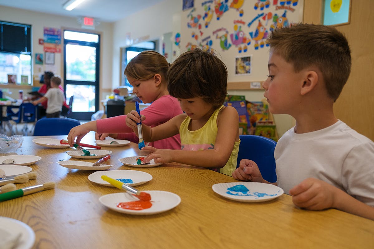 Three children painting at a table in a classroom