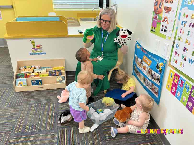 Adult holding puppets and four children gathered around in a classroom