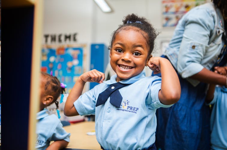 Child in uniform flexing arms in a classroom