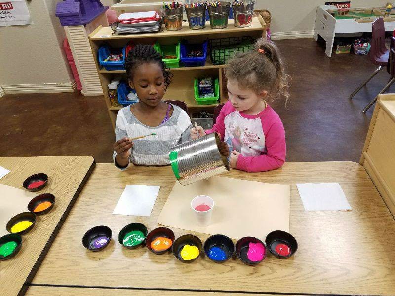 Two children painting at a table with small bowls of paint