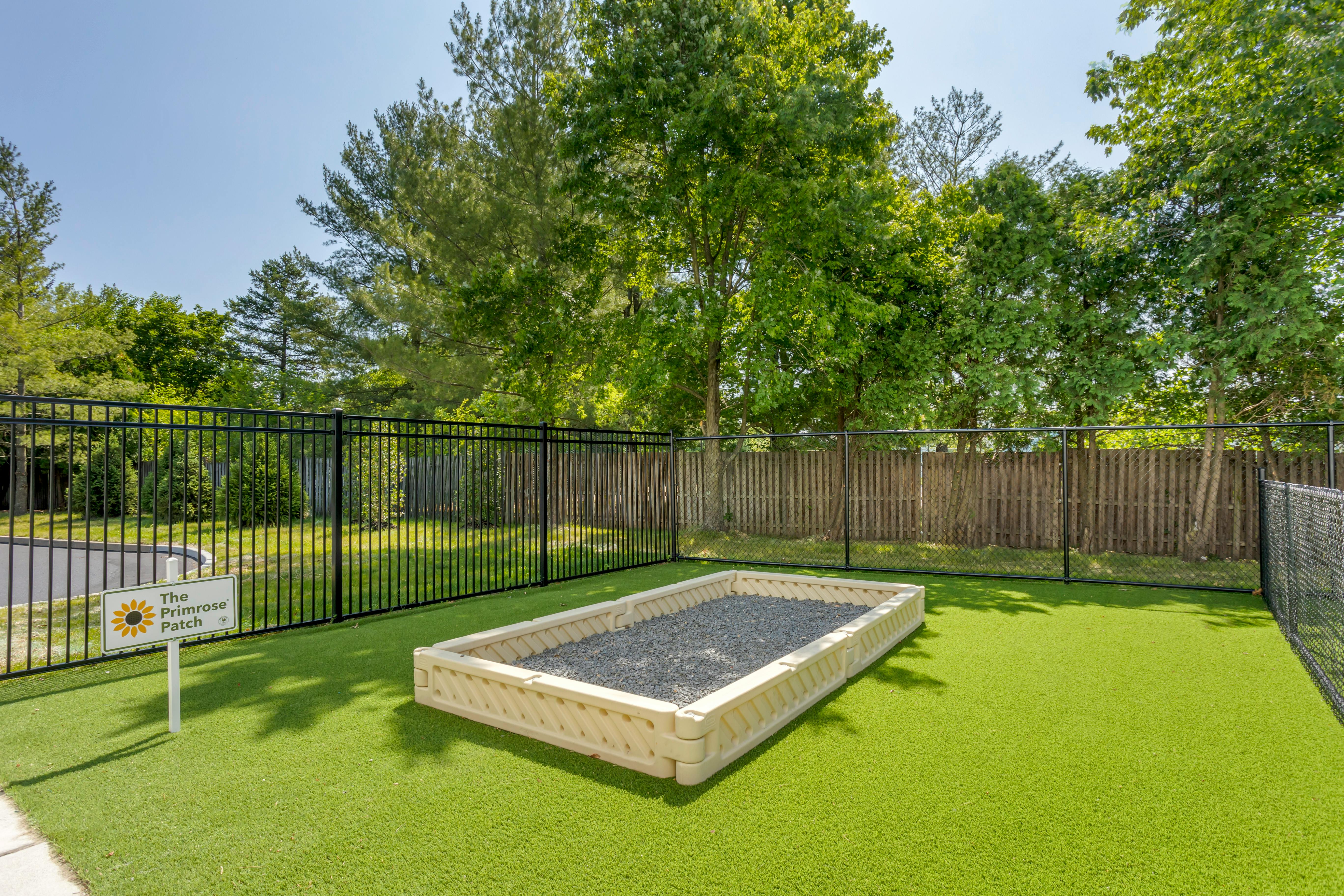 Fenced artificial grass area with a gravel pit and "The Primrose Patch" sign