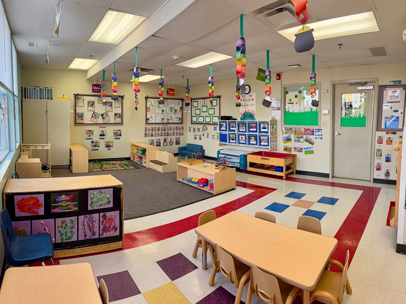A classroom with small tables and chairs, shelves, and decorations hanging from the ceiling