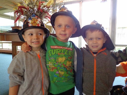 Three children wearing hats, two with firefighter hats and one with a wizard hat