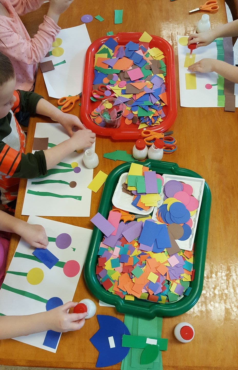 Children doing crafts with paper cutouts and glue