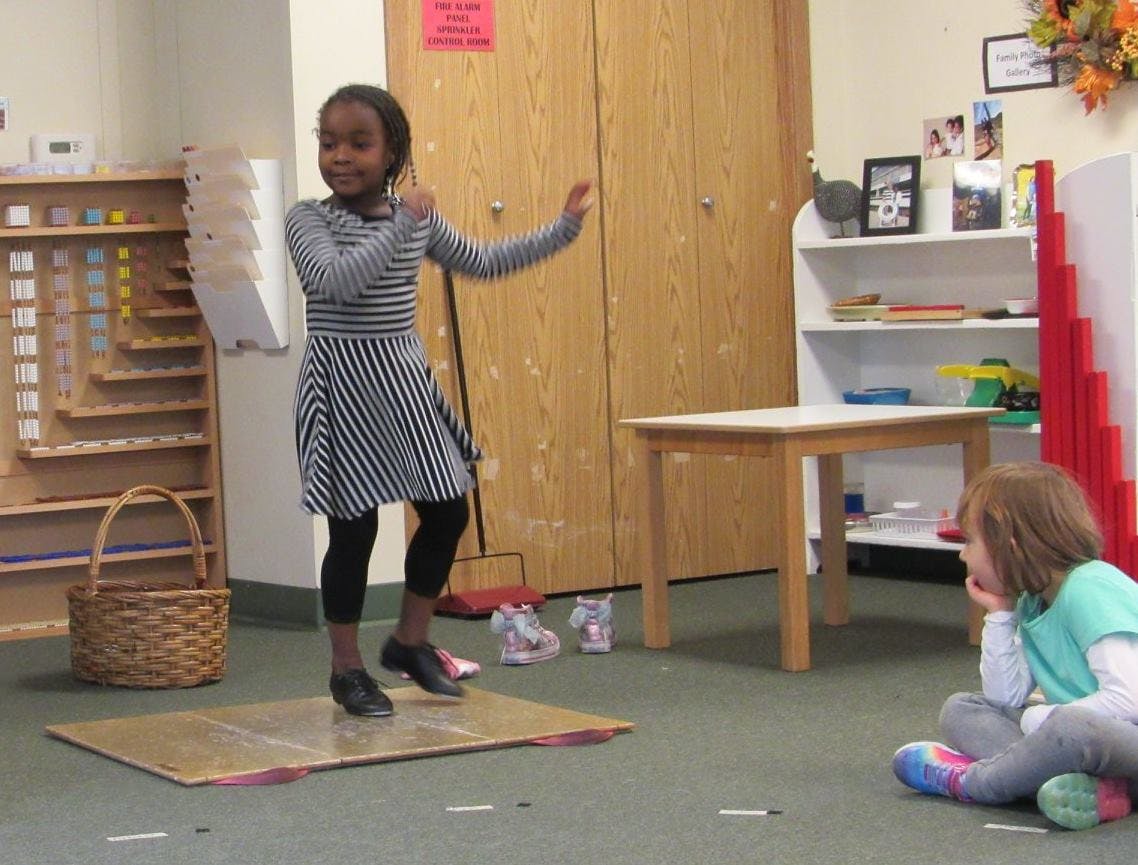 Child tap dancing on a board in a classroom while another child watches