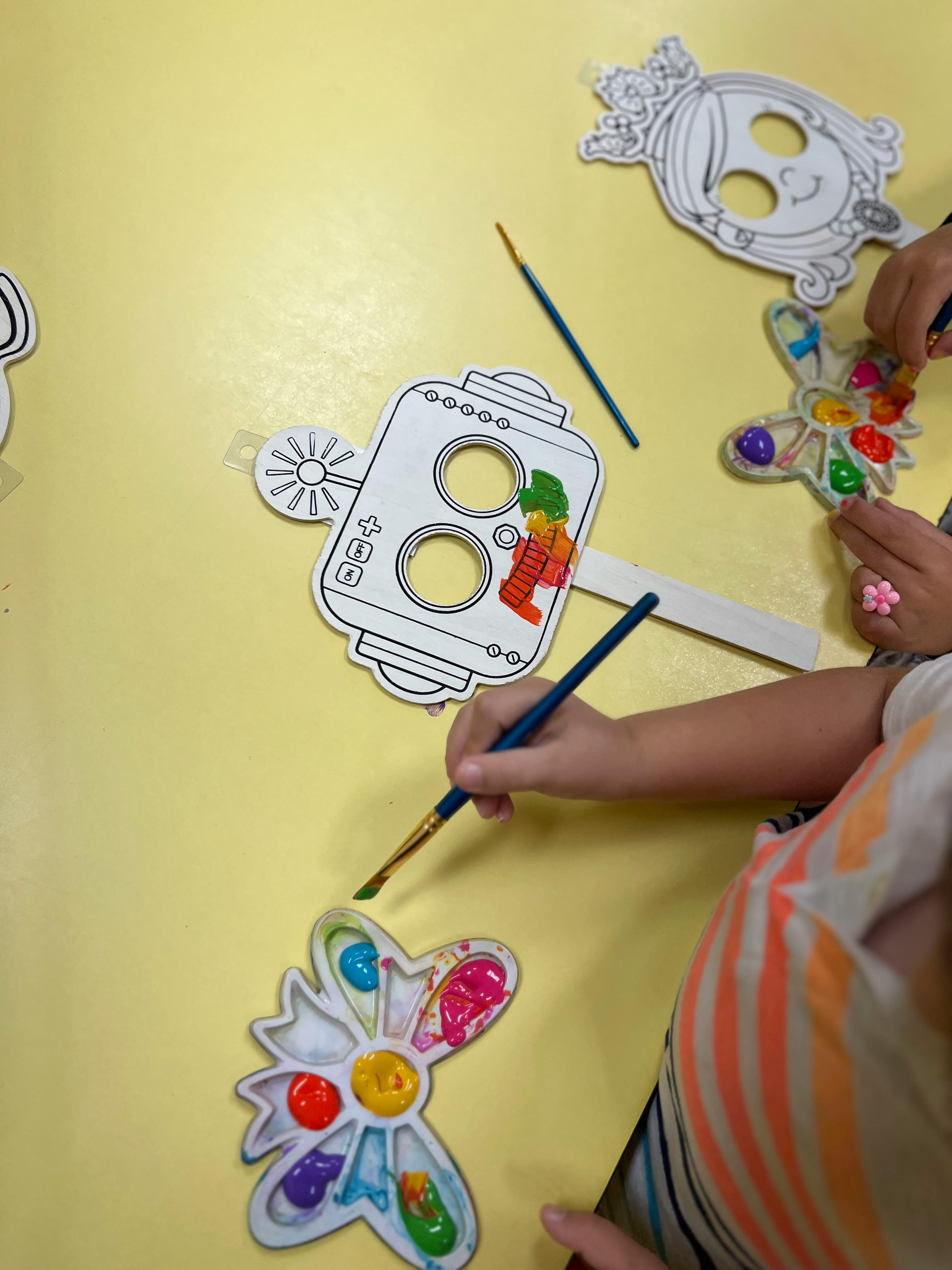 Child painting paper cutouts with brushes and colorful paints