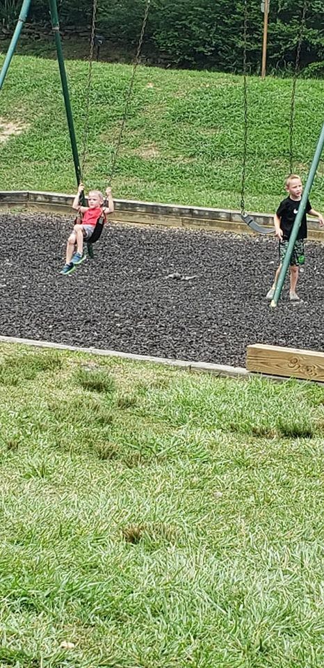 Child on a swing set, another child standing nearby