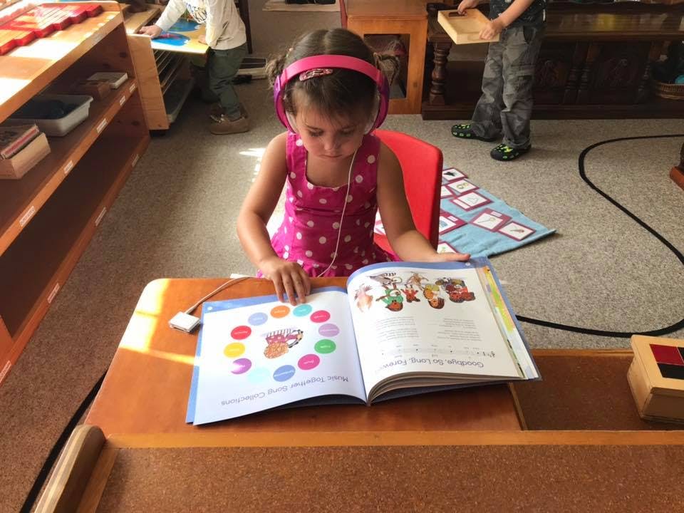 Child wearing headphones reading a book at a desk