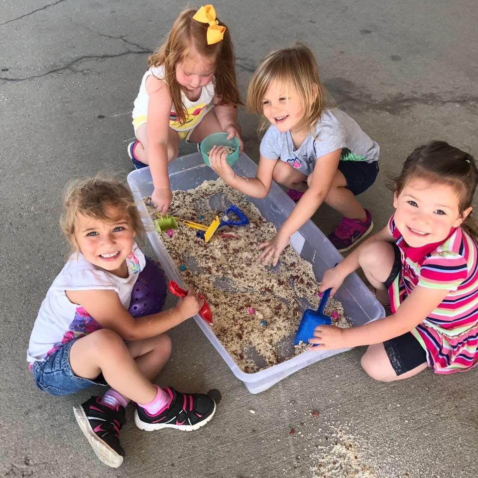 Four children playing with sand in a plastic bin