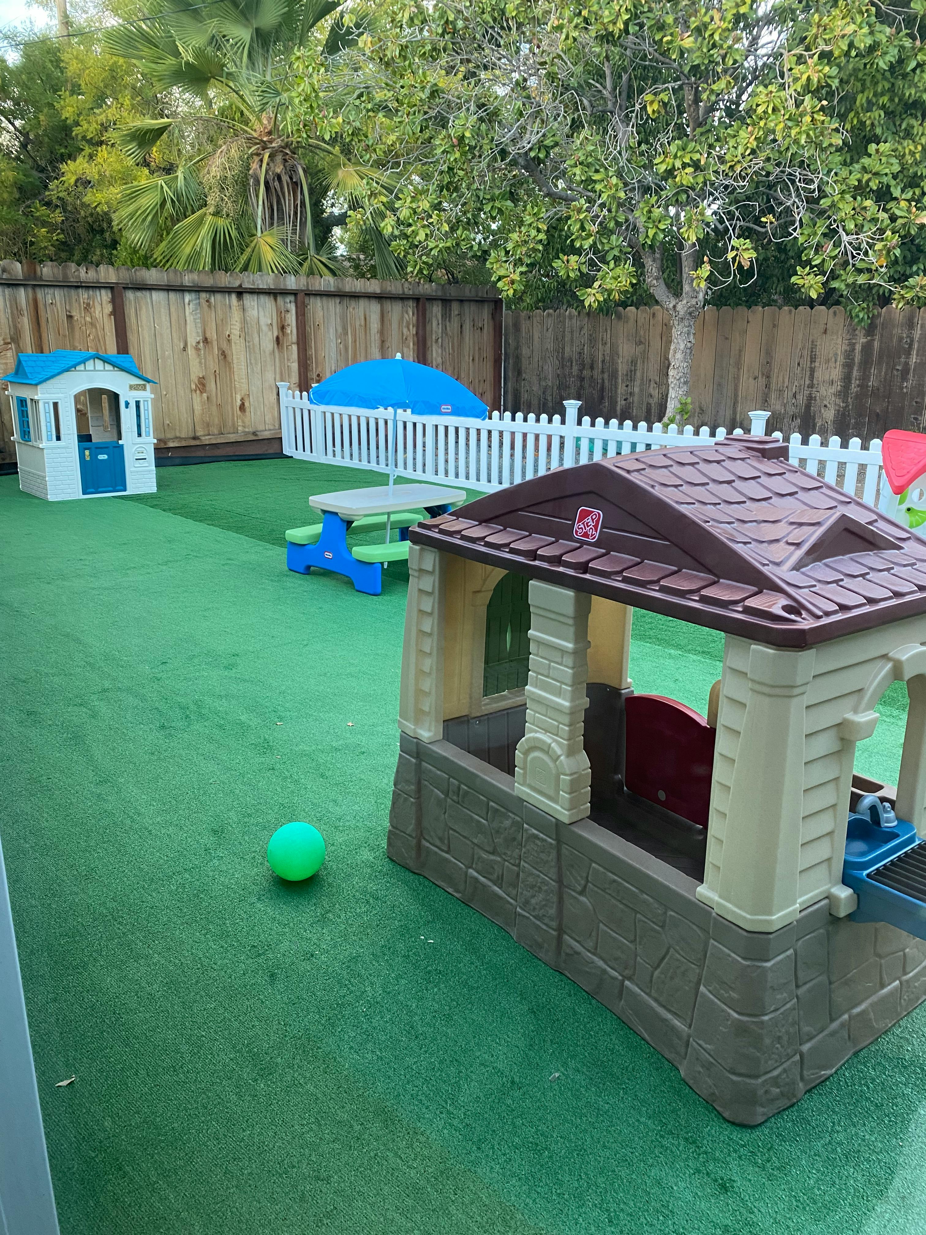 Play area with playhouses, picnic table, and green ball on artificial turf