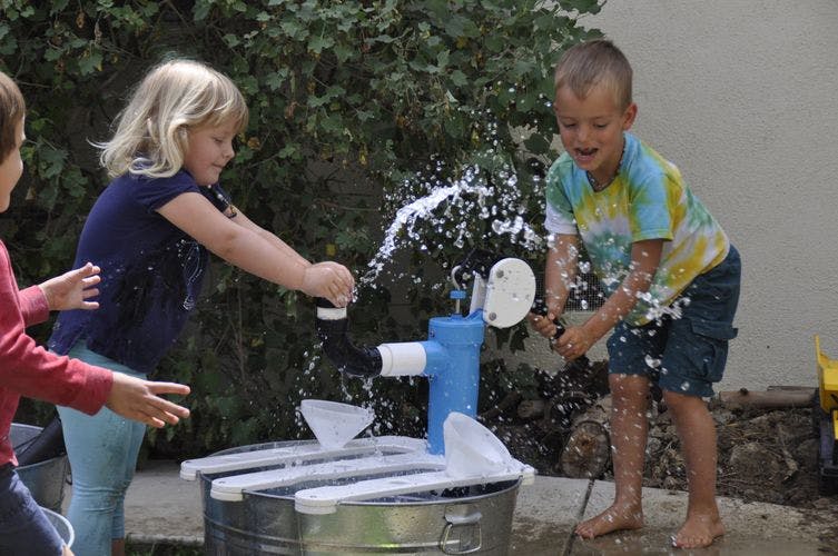 Two children playing with a water pump, splashing water