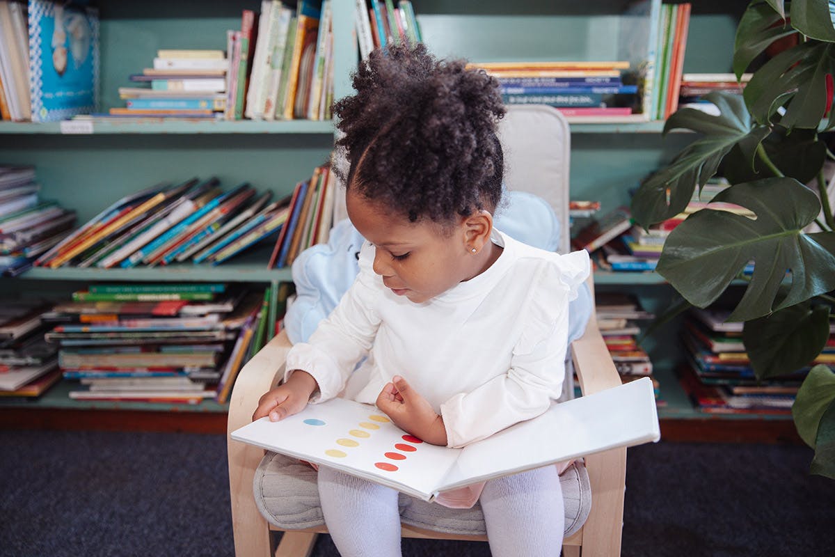 Child sitting in a chair reading a book in a library