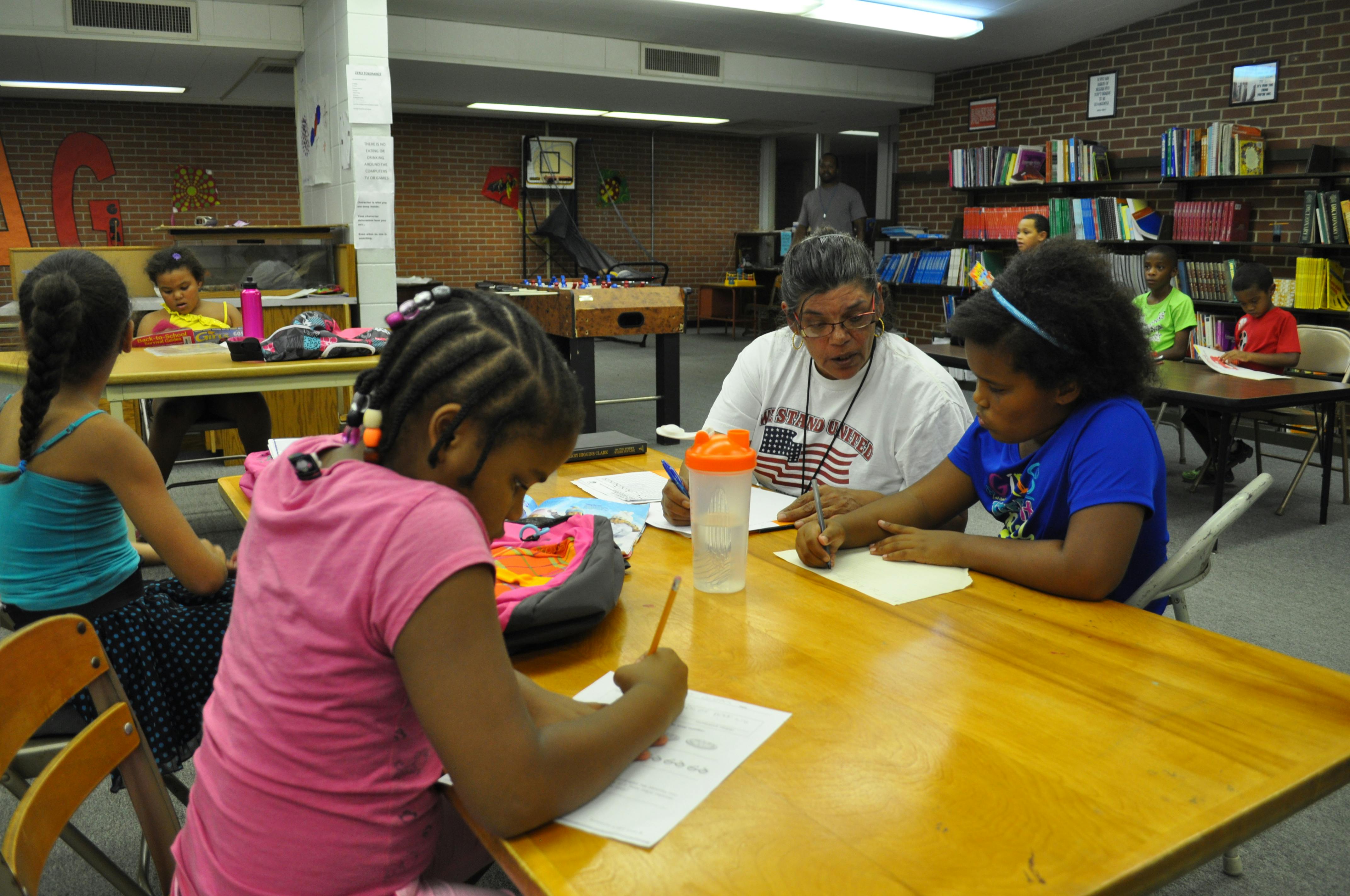 Adult and two children writing at a table in a classroom
